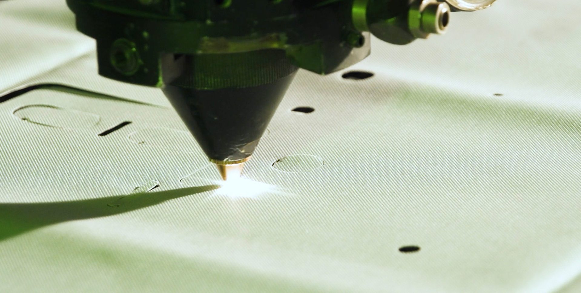 Luxinar CO₂ laser cutting head slicing intricate patterns into a white textured technical fabric