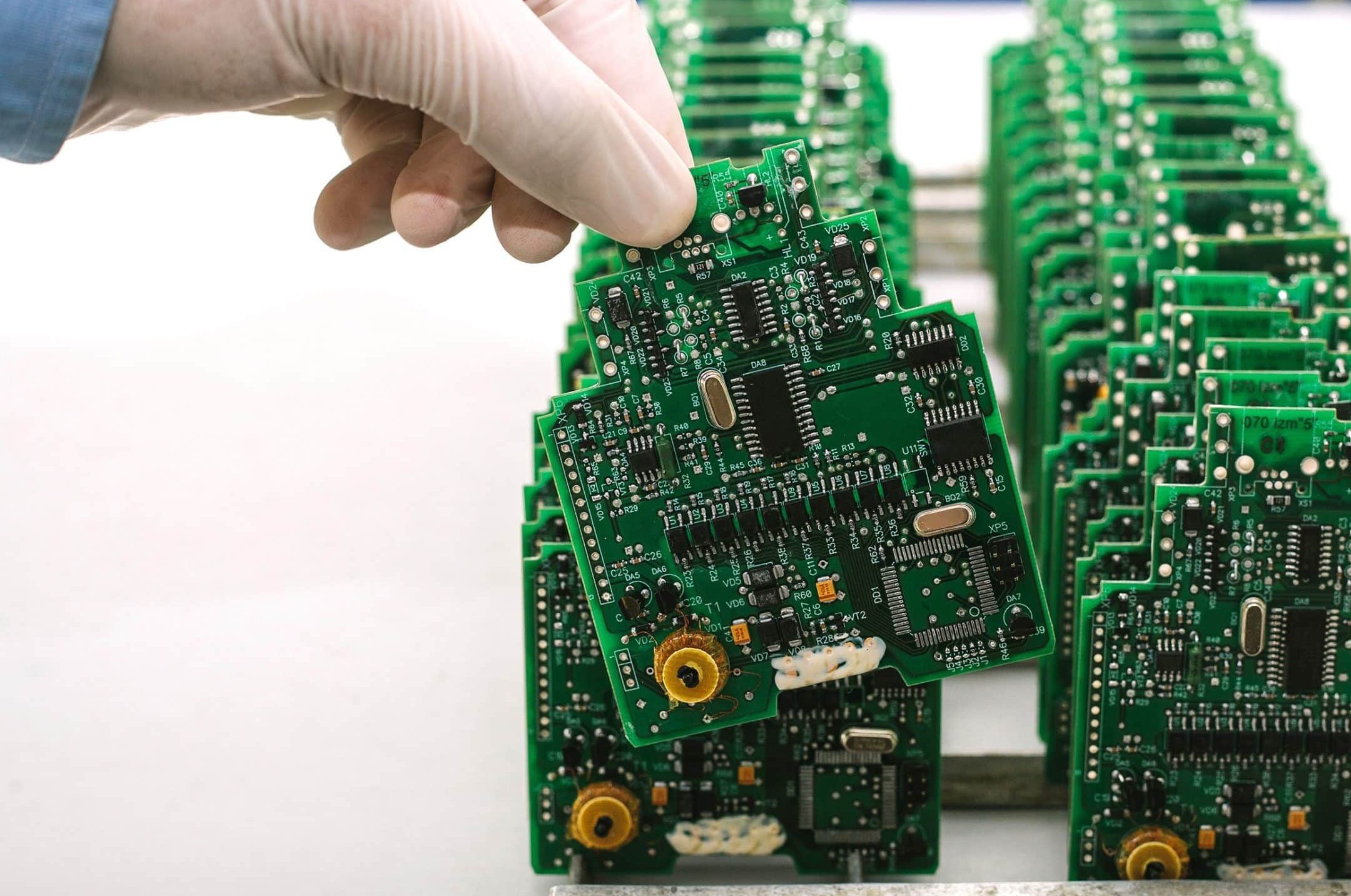 A gloved hand takes a printed circuit board out of a line-up of circuit boards