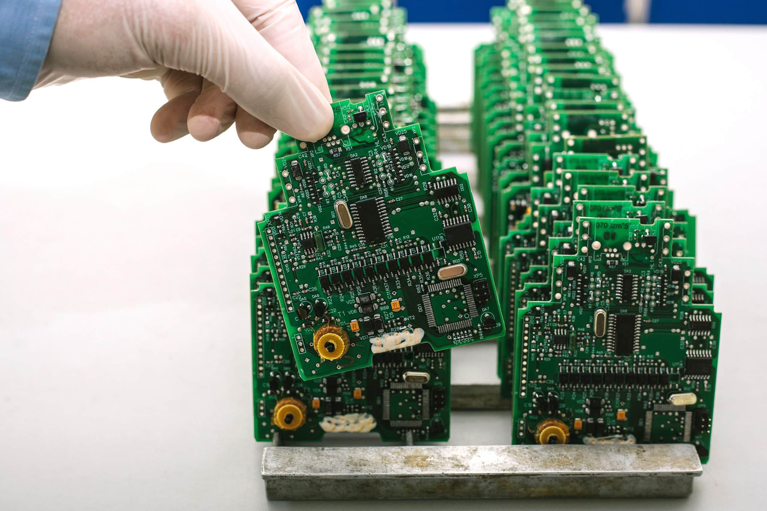 A gloved hand takes a printed circuit board out of a line-up of circuit boards