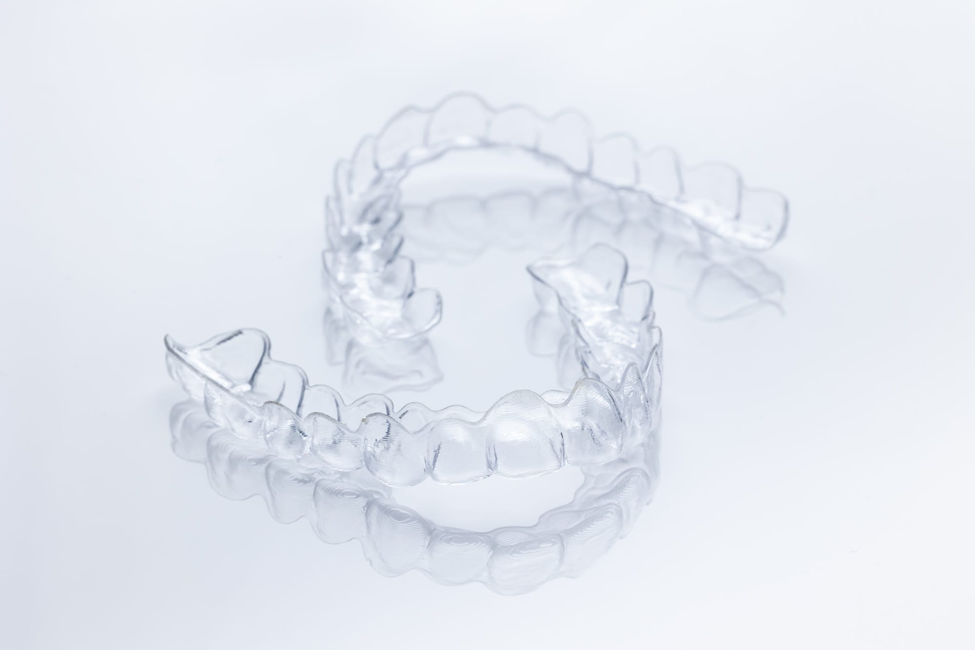 Clear transparent plastic dental aligner on a reflective white surface