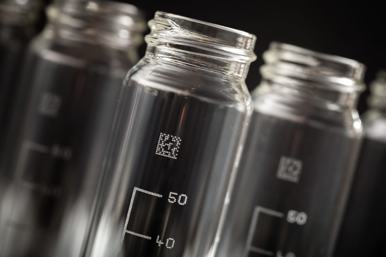 Close-up of a clear glass medical vials with laser-marked data matrix codes on the surface.