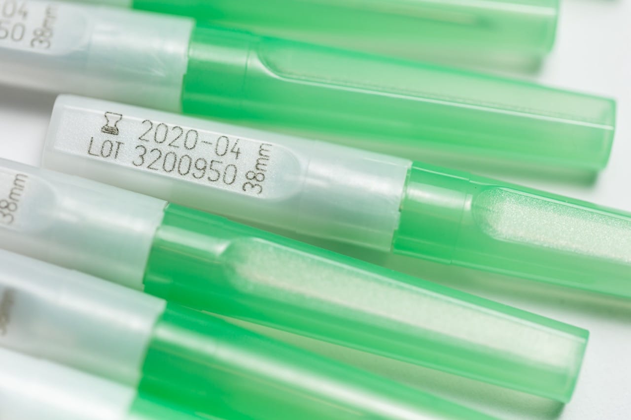 Close-up of green and white plastic syringe covers with CO2 laser-marked lot number, date and size information