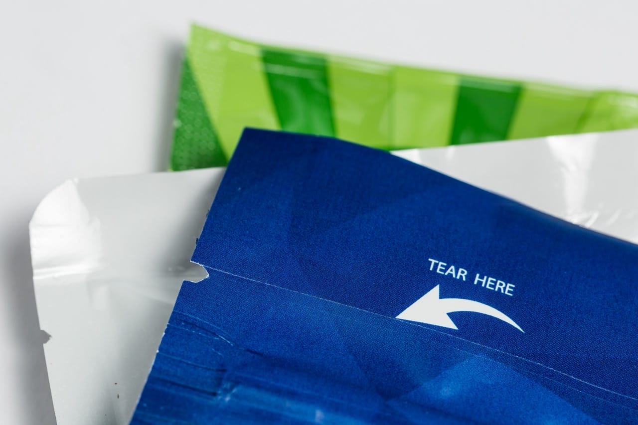 Close-up of a blue packaging pouch with a straight laser scribed tear line and “TEAR HERE” arrow