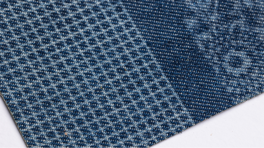 Close-up of blue denim fabric with a laser marked pattern, showing the contrast between treated and untreated areas of the textile
