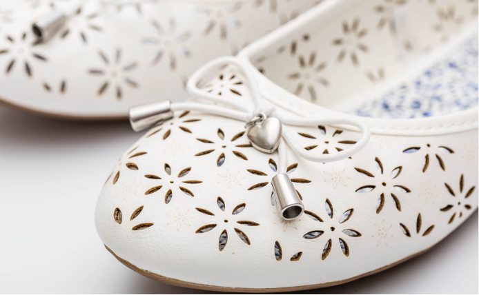 close-up of white leather ballet flat shoes featuring laser-cut floral perforations and delicate engravings