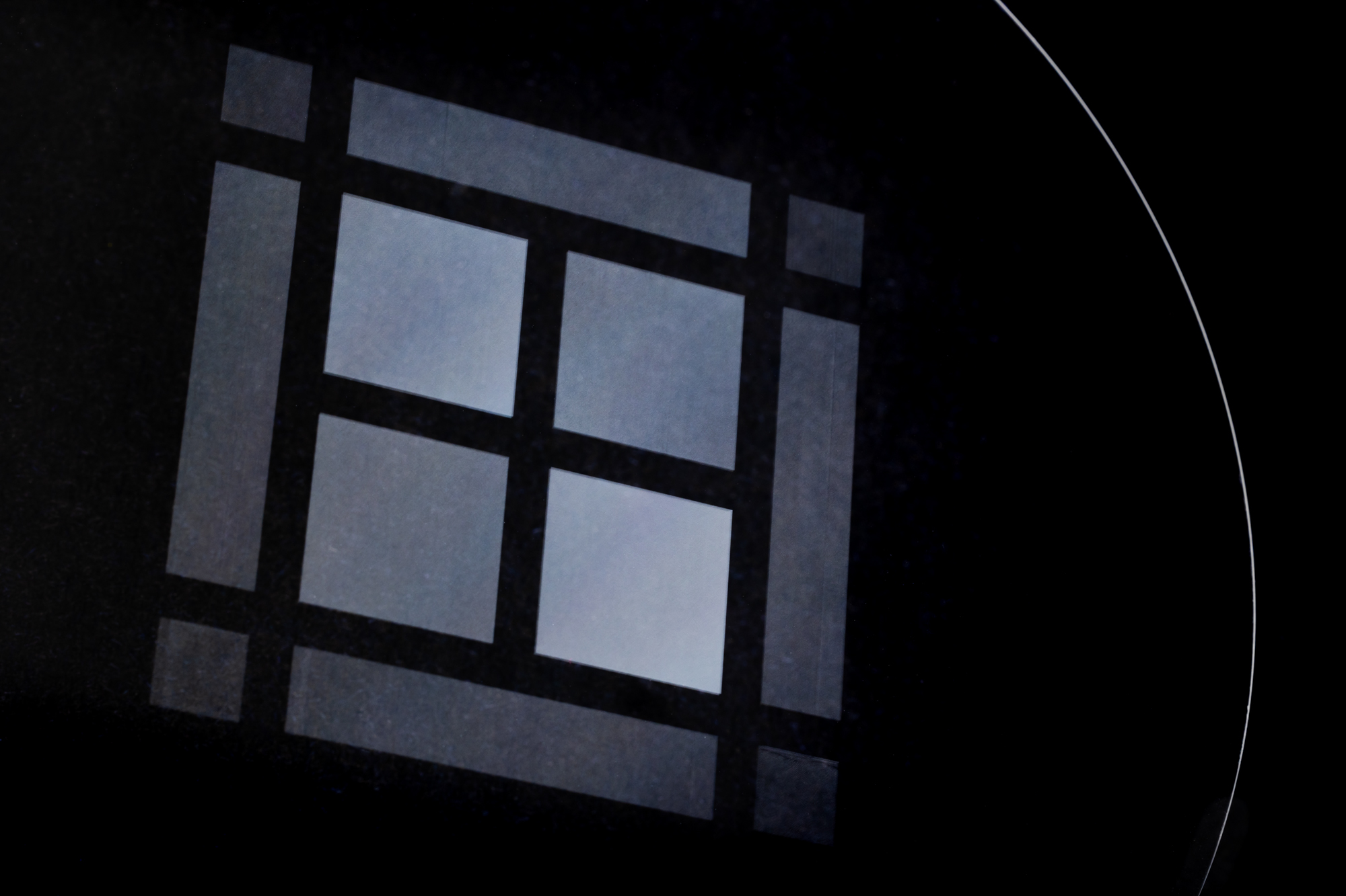 Close-up of a semiconductor wafer with precisely arranged rectangular microstructures on a dark surface.