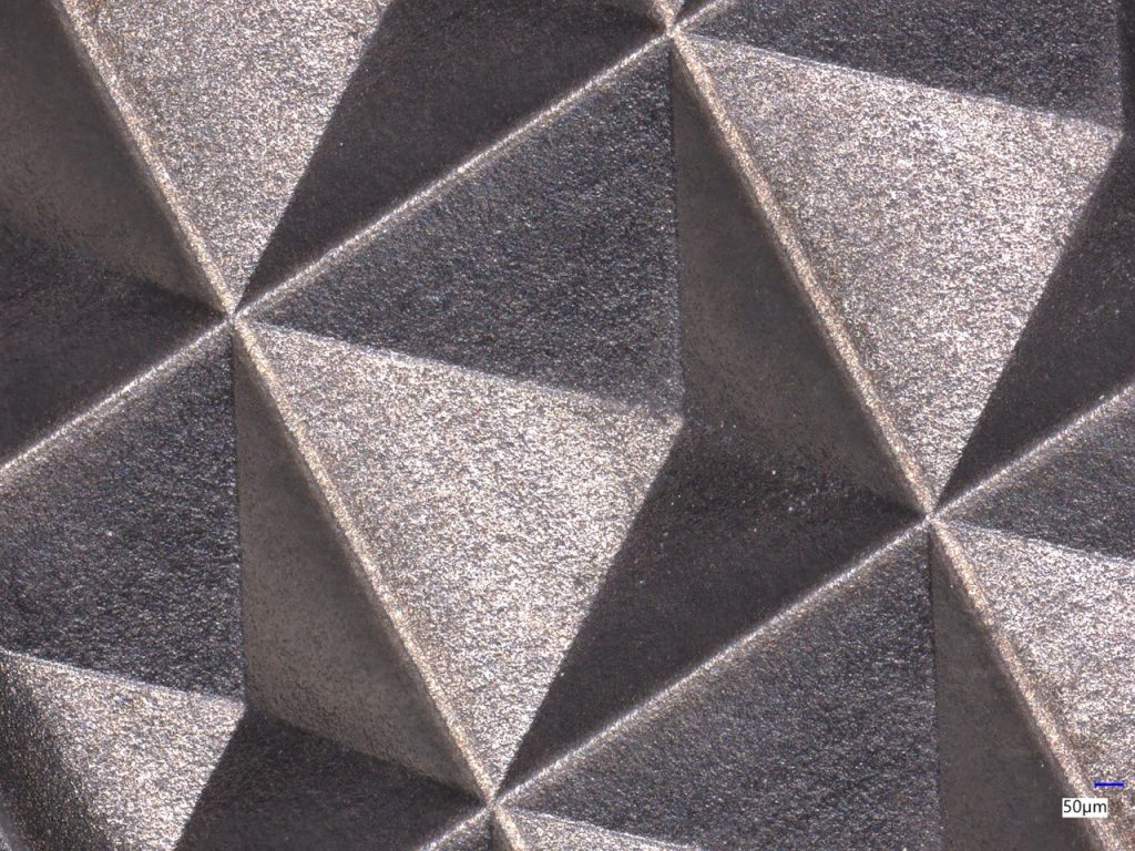 Microscopic view of a precision-engraved PCD surface with geometric patterns and a 50 µm scale bar.
