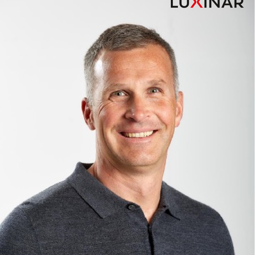 Portrait of a smiling man with short hair wearing a dark polo shirt against a light background.