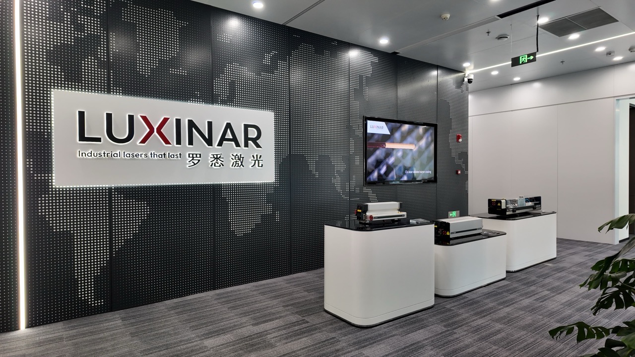 A photo of a company’s reception area featuring a wall displaying the brand logo, a white reception desk and a wall-mounted screen.