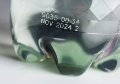 Laser marking on PET bottle with production code and date in food industry Close-up of a transparent PET bottle with laser marked production code and date