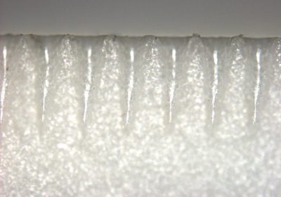 Close-up of a brittle material edge with a row of evenly spaced laser scribe marks and micro-grooves, used for controlled scribe-and-break separation in the microelectronic industry