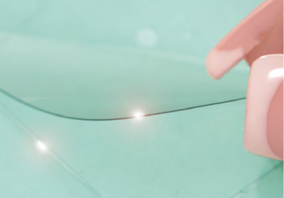 Close-up of a hand holding a transparent thin film on a teal surface, showing a clean curved cut line